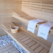 Wnętrze sauny z ławami z drewna abachi – wiadro, chochla i ręczniki