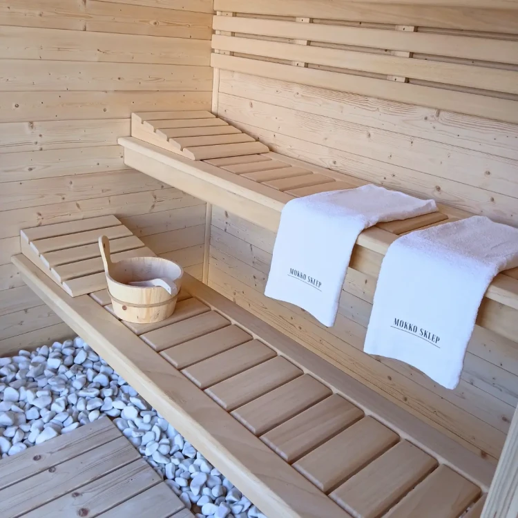 Wnętrze sauny z ławami z drewna abachi – wiadro, chochla i ręczniki